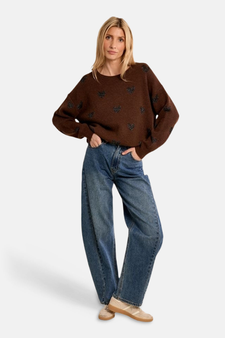 Brown O-neck sweater with black heart patterns, worn with wide-leg blue jeans and beige sneakers, front view