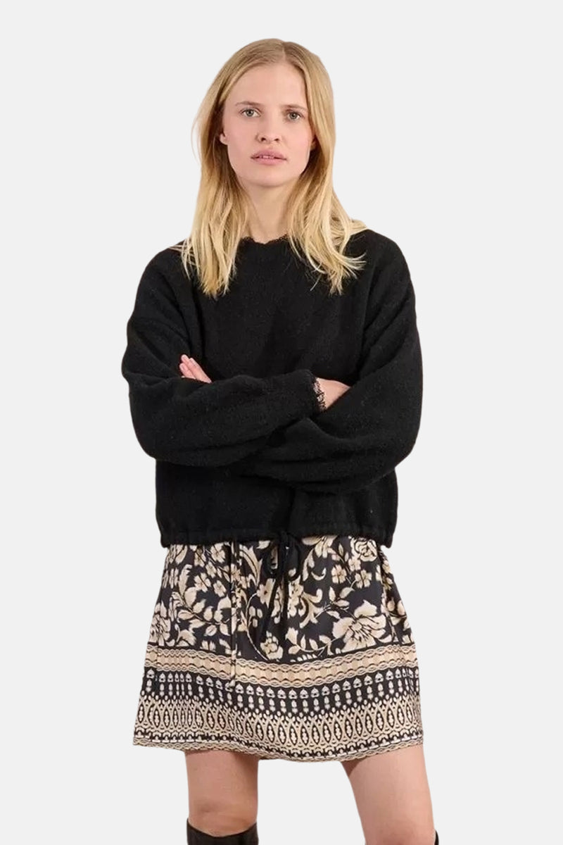 Pull à col rond noir de Molly Bracken, porté avec une jupe à motif floral et bordure décorative.