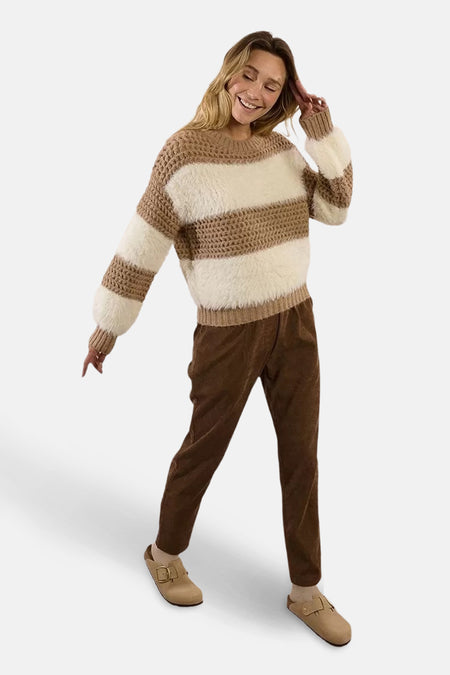 Multikleuren rondehals trui van Molly Bracken, met horizontale strepen, gedragen met een bruine broek en klompen.