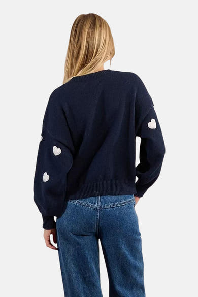 Pull ras du cou bleu marine de Molly Bracken, orné de motifs de cœur blancs sur les manches.