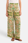 Pantalon large multicolore de Molly Bracken à motif cachemire et géométrique vert, orange et crème, porté avec un t-shirt blanc et des sandales.