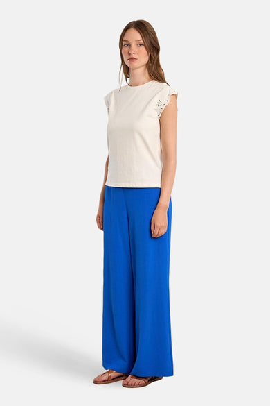 Witte T-shirt van Molly Bracken met uitgesneden details op de schouders, gedragen met een wijde blauwe broek en leren sandalen.