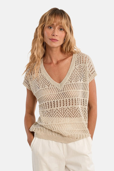 Zilveren V-hals trui van Molly Bracken, in ajour gebreid met geometrische patronen, gedragen met een witte broek.