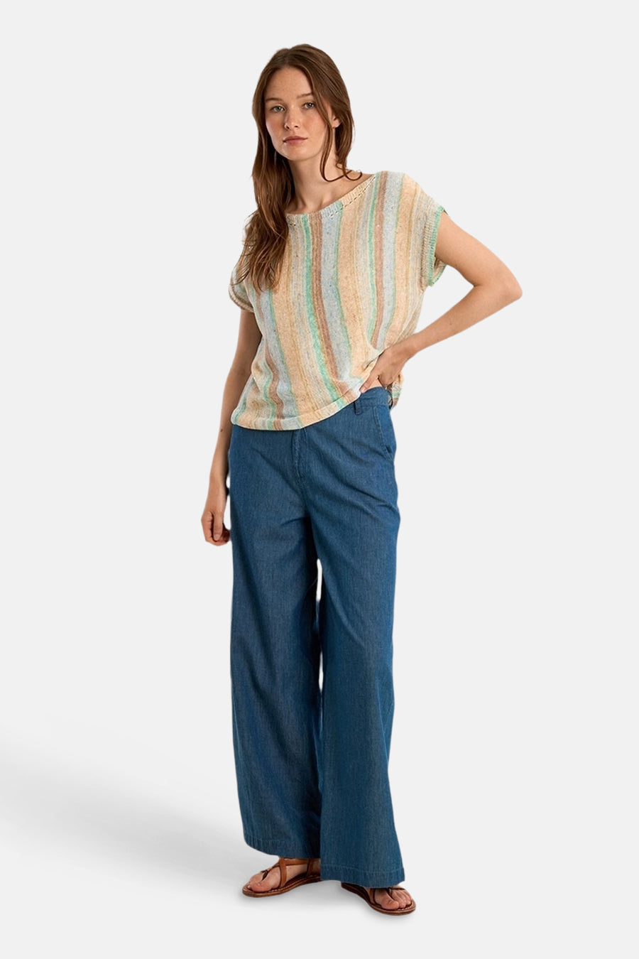 Molly Bracken meerkleurige trui met verticale strepen, gedragen met een wijde blauwe broek en bruine sandalen.