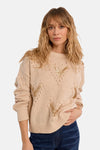 Beige crewneck sweater with gold sequin V-patterns and textured knit, worn with dark blue jeans, front view