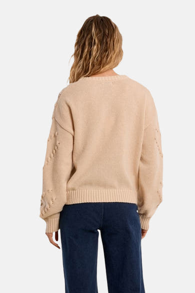 Beige crewneck sweater with textured knit and decorative eyelet details on sleeves, back view, worn with dark blue jeans