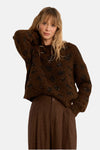 Brown O-neck sweater with black sequin floral pattern, soft textured knit, worn with matching pleated trousers, front view.