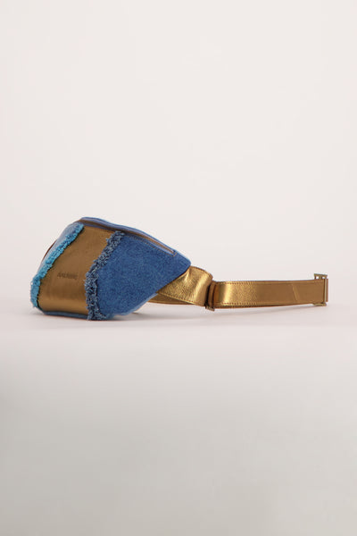 Blauwe handtas van PAUL MARIUS, met spijkerstof inzetten en franjedetails, aan de riem gedragen.