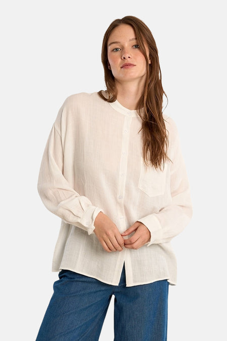 Chemisier blanc à manches longues de Molly Bracken, avec une poche poitrine, porté avec un pantalon en denim bleu.