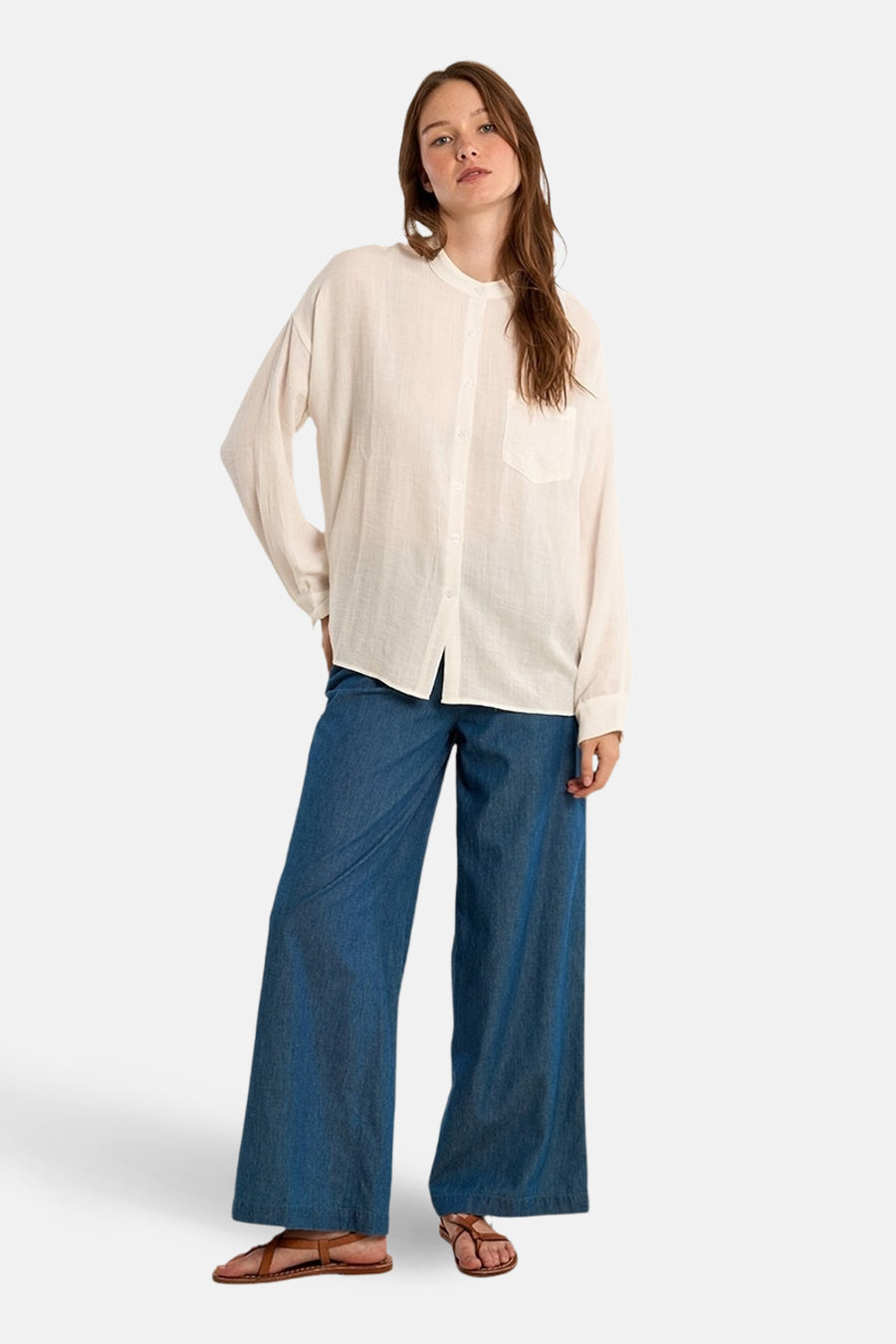 Chemisier blanc à manches longues de Molly Bracken, porté avec un pantalon large en denim bleu et des sandales en cuir marron.