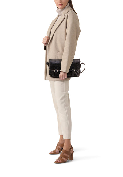 Sac à bandoulière noir de PAUL MARIUS, porté à la main avec un manteau beige et un pantalon blanc.