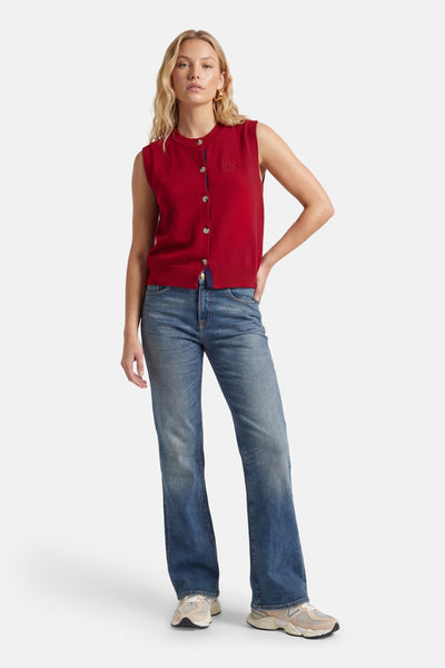 Gilet rouge d'ADORE avec boutons, porté avec un jean bleu et des baskets beiges.
