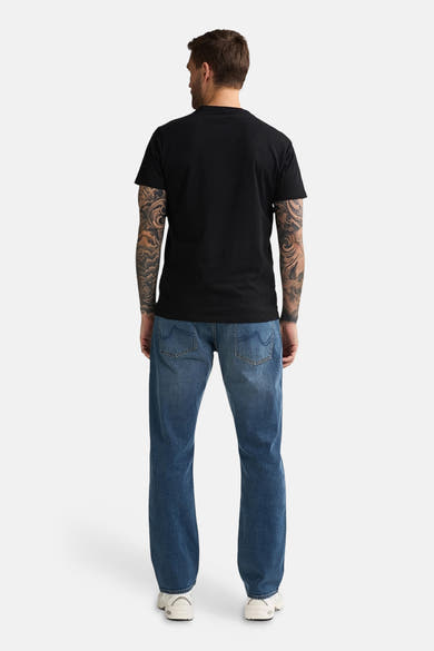 Mid blue denim jeans by LEWIS, back view, relaxed fit with classic stitching and two rear pockets, worn with black t-shirt and white sneakers