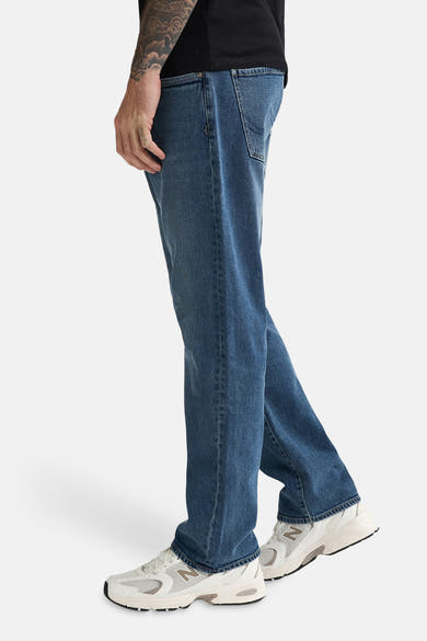 Mid blue denim jeans by LEWIS, side view, relaxed fit with visible stitching and worn texture, paired with white sneakers