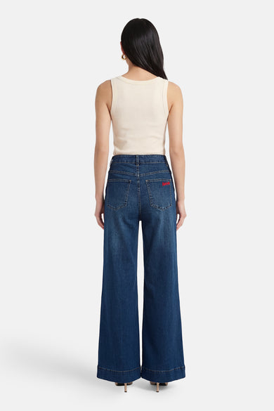 Jean large en denim bleu moyen par ADORE avec une inscription rouge sur la poche arrière.