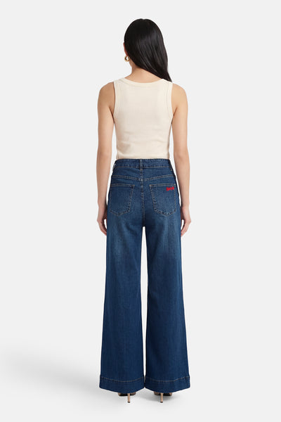 Jean large en denim bleu moyen par ADORE avec une inscription rouge sur la poche arrière.