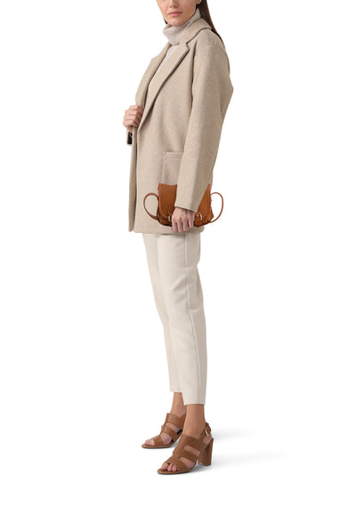 Brown leather handbag with curved handles and front buckle, worn by model in beige blazer and cream pants, side view.