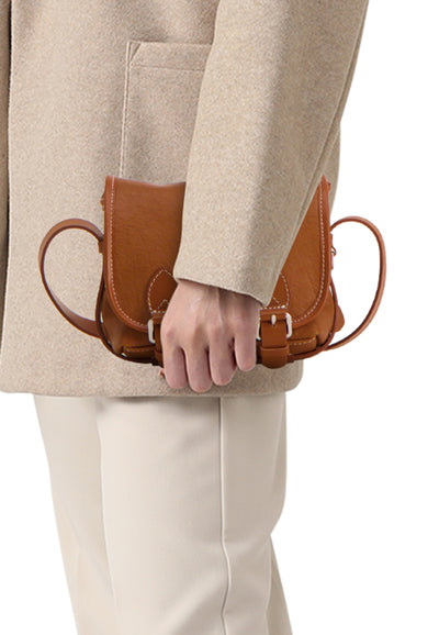 Brown leather handbag with white stitching and buckle closure, worn at waist by model in beige coat, side view