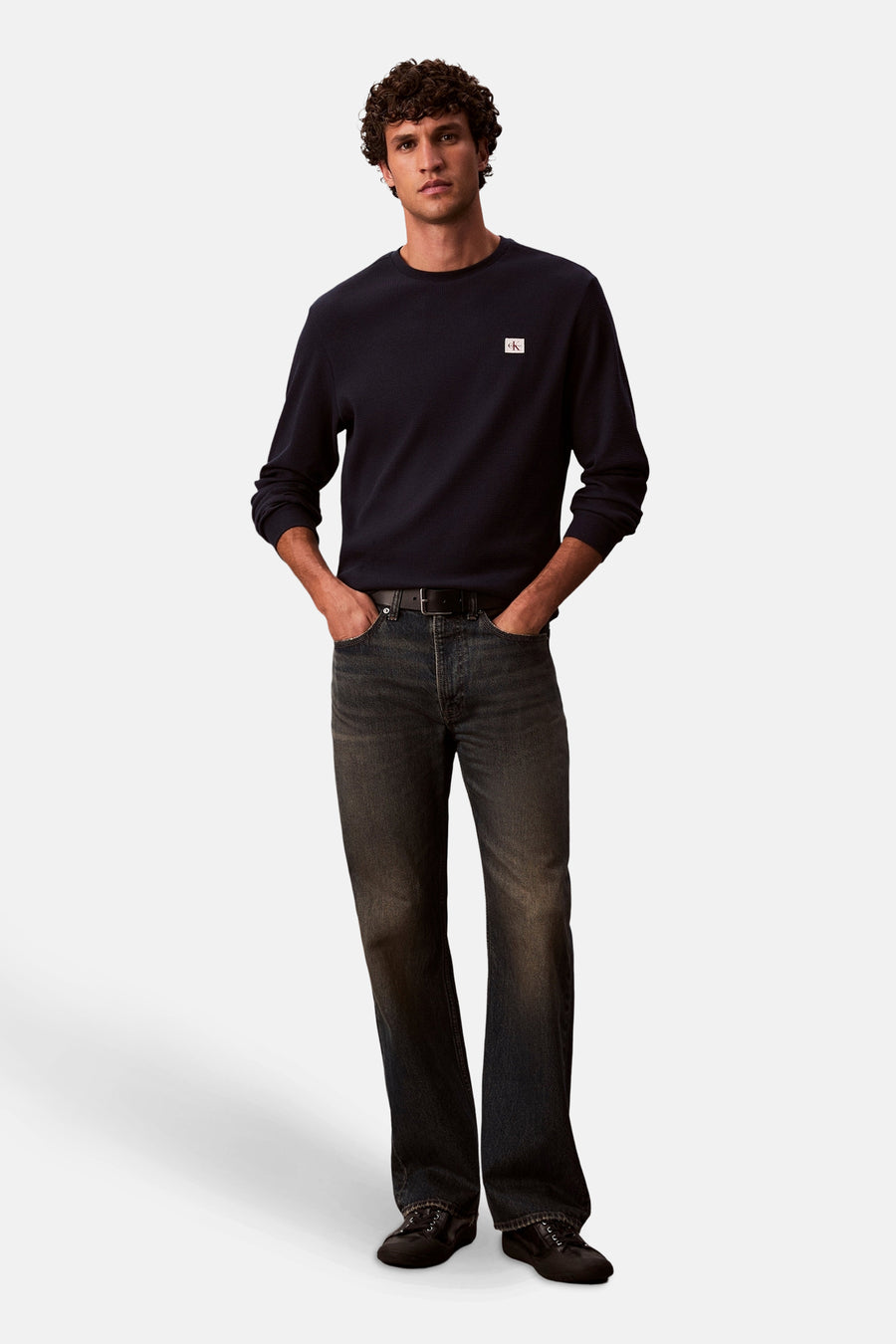 Blauw T-shirt met lange mouwen van Calvin Klein, met een klein vierkant logo op de borst. Gedragen met een donkere spijkerbroek en zwarte schoenen.