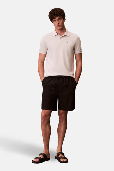 Polo écru à manches courtes de Calvin Klein, porté avec un short noir et des sandales.