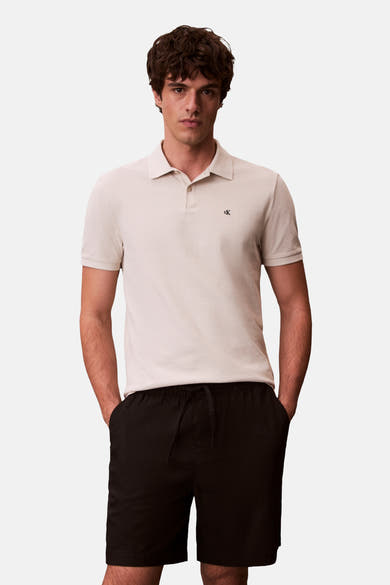 Polo à manches courtes écru de Calvin Klein, porté avec un short noir à cordon.