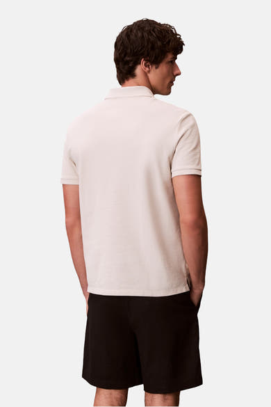 Polo écru à manches courtes de Calvin Klein, porté avec un short noir, vue de dos.
