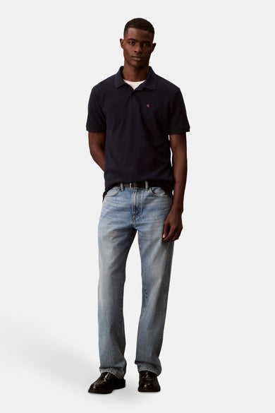 Polo bleu marine en coton, de Calvin Klein, porté avec un jean délavé, une ceinture noire et des chaussures noires.