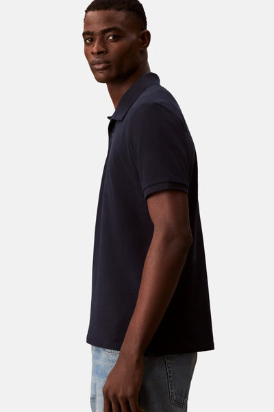 Marineblauwe Calvin Klein polo, gedragen met een lichtgewassen spijkerbroek, in zijaanzicht.