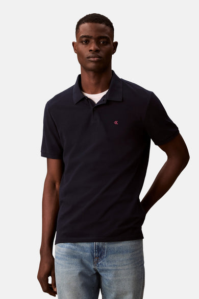 Polo bleu marine de Calvin Klein, avec un petit logo rose sur le devant, porté avec un jean clair.
