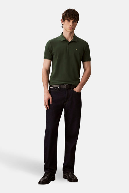 Groen poloshirt met korte mouwen van Calvin Klein, gedragen met een donkerblauwe spijkerbroek en zwarte nette schoenen.