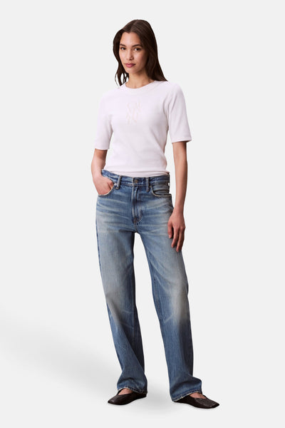 T-shirt blanc à manches courtes de Calvin Klein, porté avec un jean décontracté bleu et des chaussures plates noires.