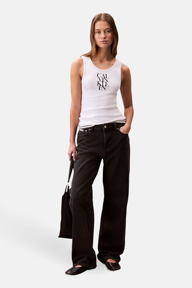 Débardeur blanc de Calvin Klein, porté avec un jean noir ample et des chaussures plates noires, tenant un sac à main.
