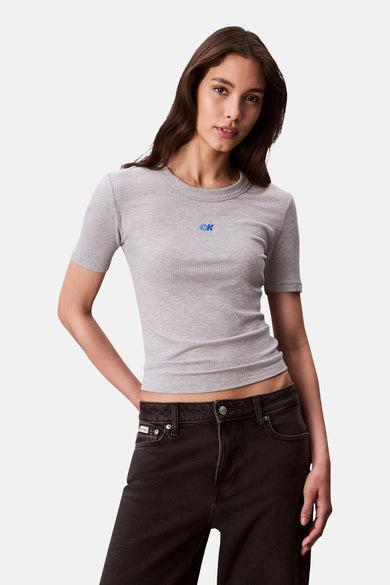 T-shirt gris côtelé à manches courtes de Calvin Klein, avec un logo bleu sur la poitrine, porté avec un jean noir.