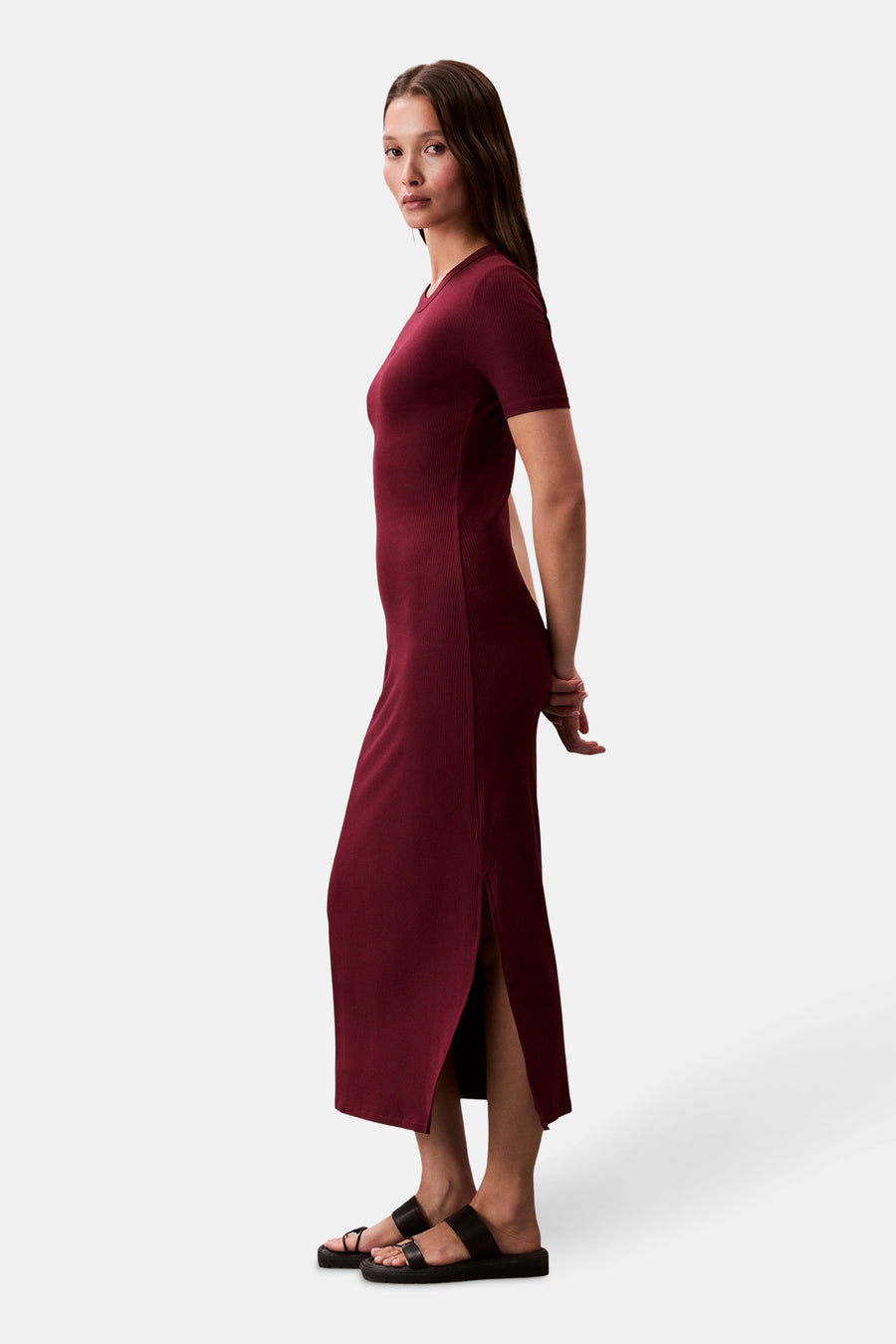 Robe longue bordeaux par Calvin Klein, coupe moulante avec fente latérale et portée avec des sandales à plateforme noires.