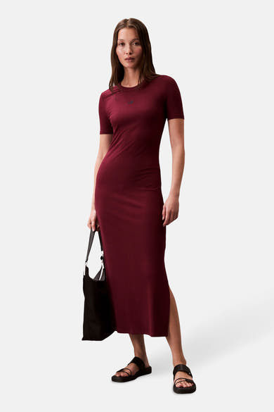 Robe longue bordeaux côtelée de Calvin Klein, avec des manches courtes et une fente latérale, portée avec des sandales noires.
