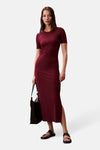 Robe longue bordeaux côtelée de Calvin Klein, avec des manches courtes et une fente latérale, portée avec des sandales noires.