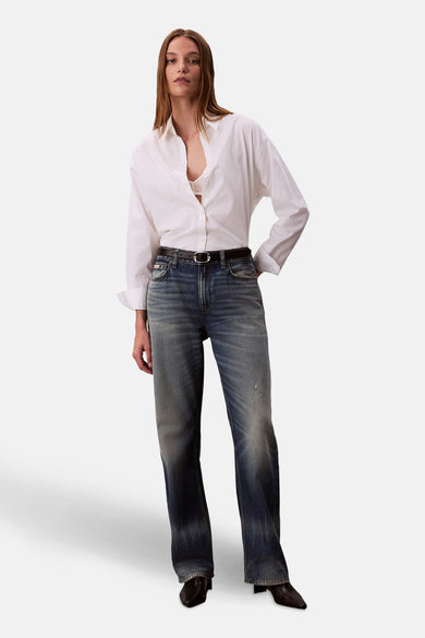 Wit Calvin Klein overhemd met lange mouwen, open gedragen met een zichtbare kanten beha en een blauwe spijkerbroek.