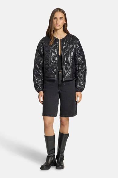 Korte zwarte Calvin Klein jas, gewatteerd met een geometrisch patroon, gedragen met een spijkerbroekje en leren laarzen.