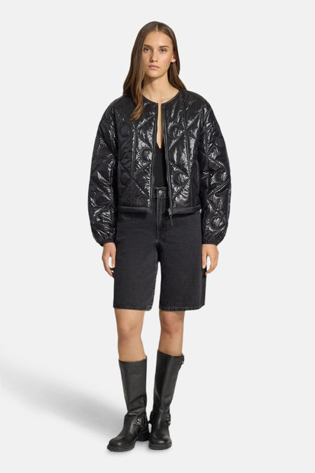 Korte zwarte Calvin Klein jas, gewatteerd met een geometrisch patroon, gedragen met een spijkerbroekje en leren laarzen.