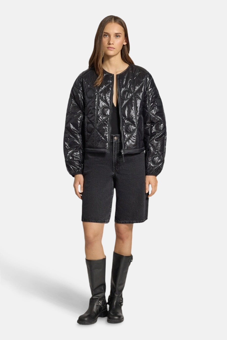 Korte zwarte Calvin Klein jas, gewatteerd met een geometrisch patroon, gedragen met een spijkerbroekje en leren laarzen.