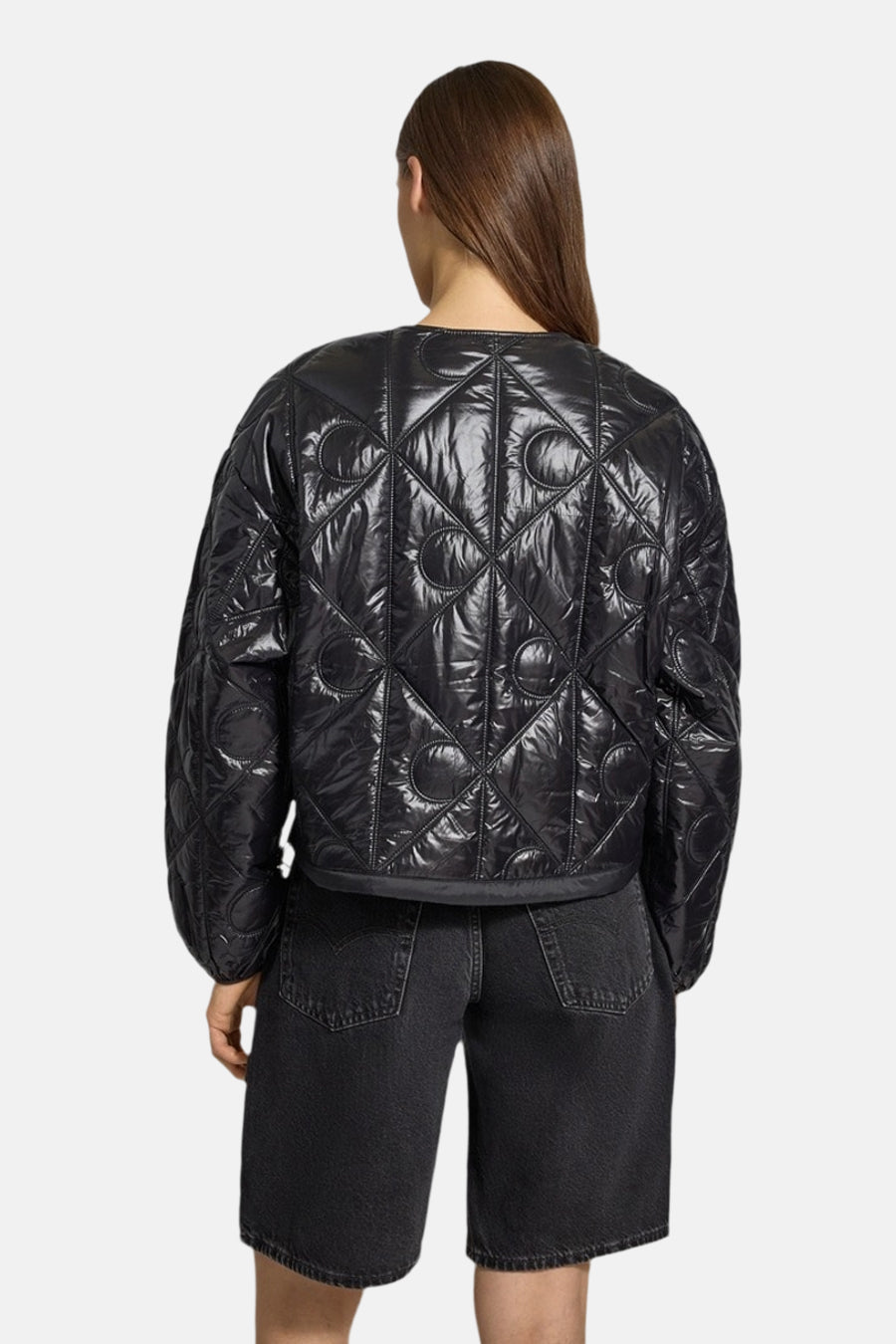 Korte zwarte gewatteerde jas van Calvin Klein, met ruit- en halvemaanpatroon, gedragen met een zwarte spijkerbroekshort, van achteren gezien.