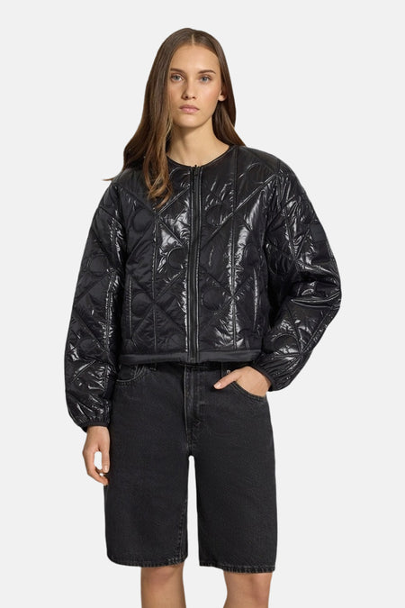 Korte zwarte gewatteerde jas van Calvin Klein, met ruitpatroon en centrale ritssluiting, gedragen met een zwarte spijkerbroek met korte pijpen.