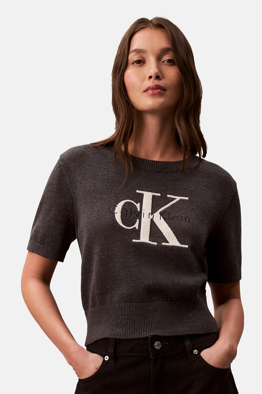 Pull gris à col rond de Calvin Klein, avec logo blanc, porté avec un pantalon sombre.
