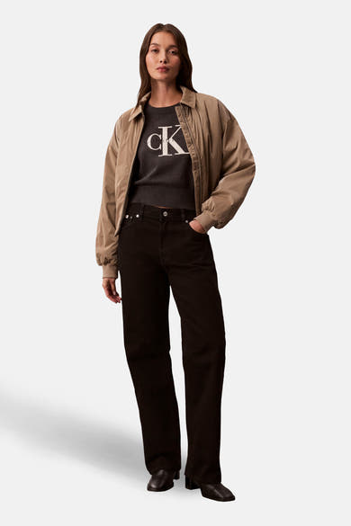 Pull à col rond gris de Calvin Klein, avec logo blanc, porté avec une veste et un pantalon noirs.