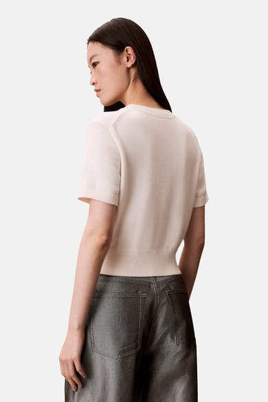 Pull à col rond écru de Calvin Klein, porté avec un pantalon brillant, vue de dos.
