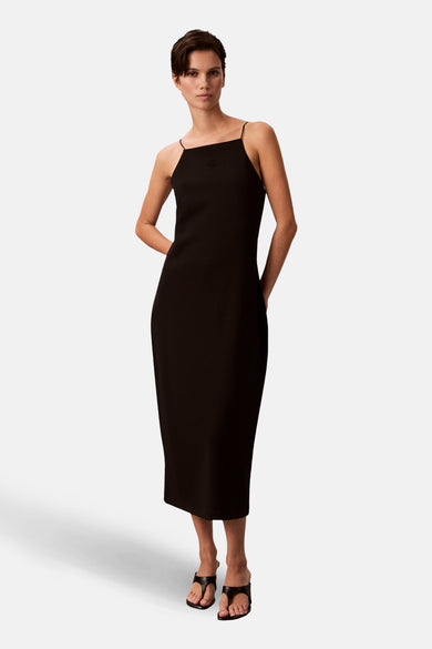 Eenvoudige zwarte jurk van Calvin Klein, midi-model met dunne bandjes en hakken.