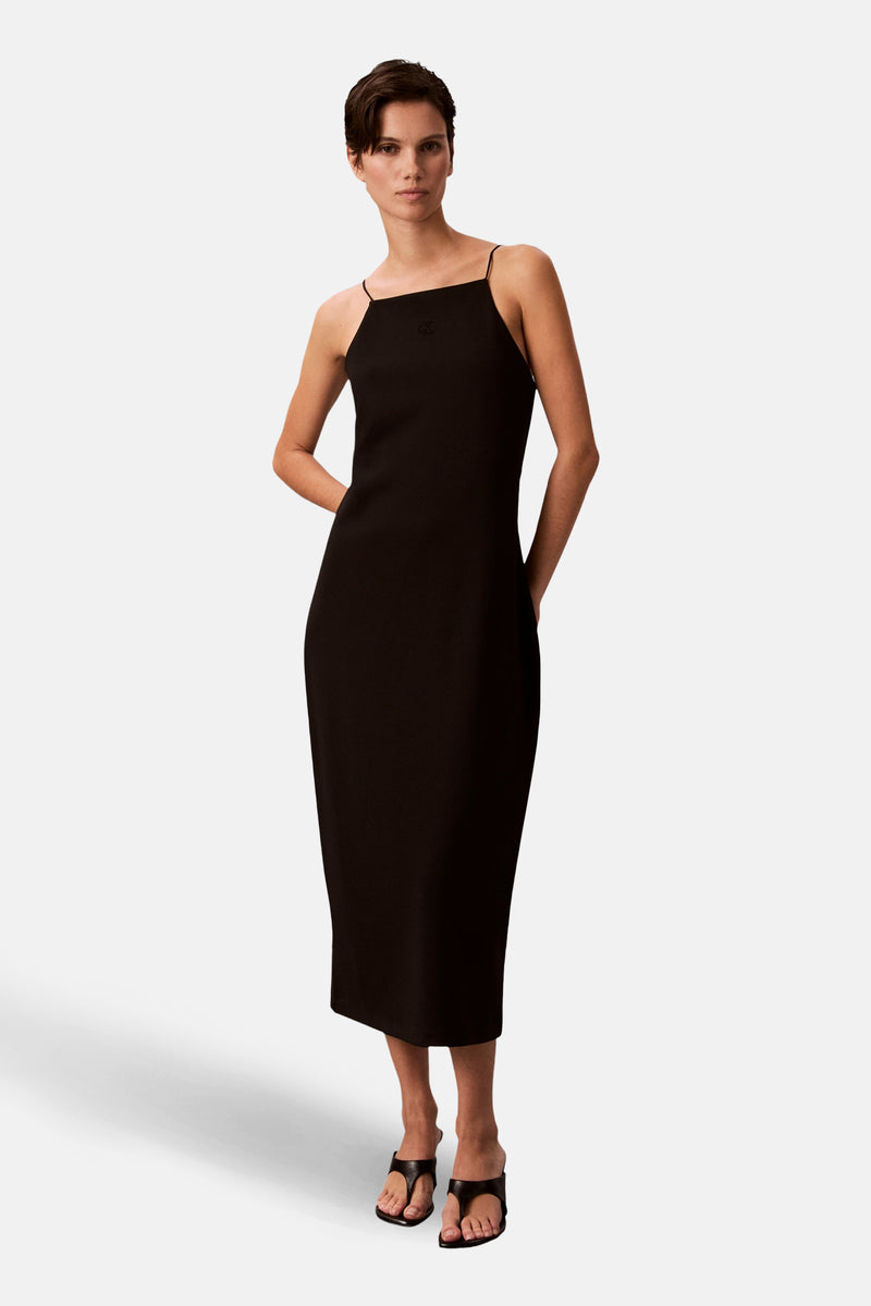 Eenvoudige zwarte jurk van Calvin Klein, midi-model met dunne bandjes en hakken.