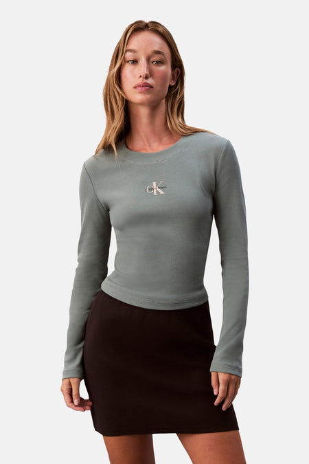 T-shirt à manches longues vert côtelé de Calvin Klein avec logo sur la poitrine, porté par un mannequin avec une jupe brune.