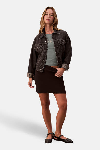 T-shirt à manches longues vert de Calvin Klein, porté avec une veste en jean noire et une jupe marron.
