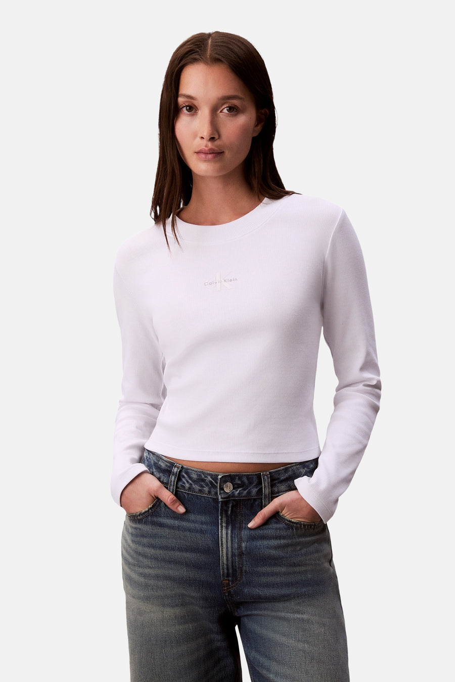Wit T-shirt met lange mouwen van Calvin Klein, gedragen met een lichtblauwe jeans, handen in de zakken.